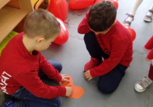 Dwóch klęczących chłopców dopasowuje połówki serca z papieru.